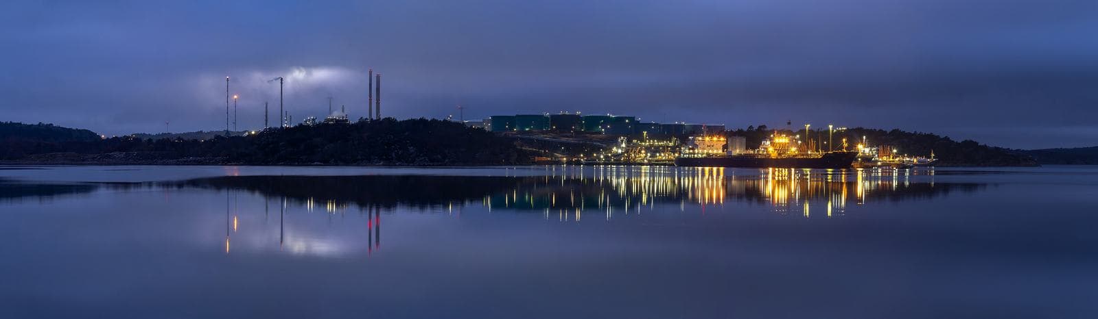 An oil refinery lit at dusk, seen across water